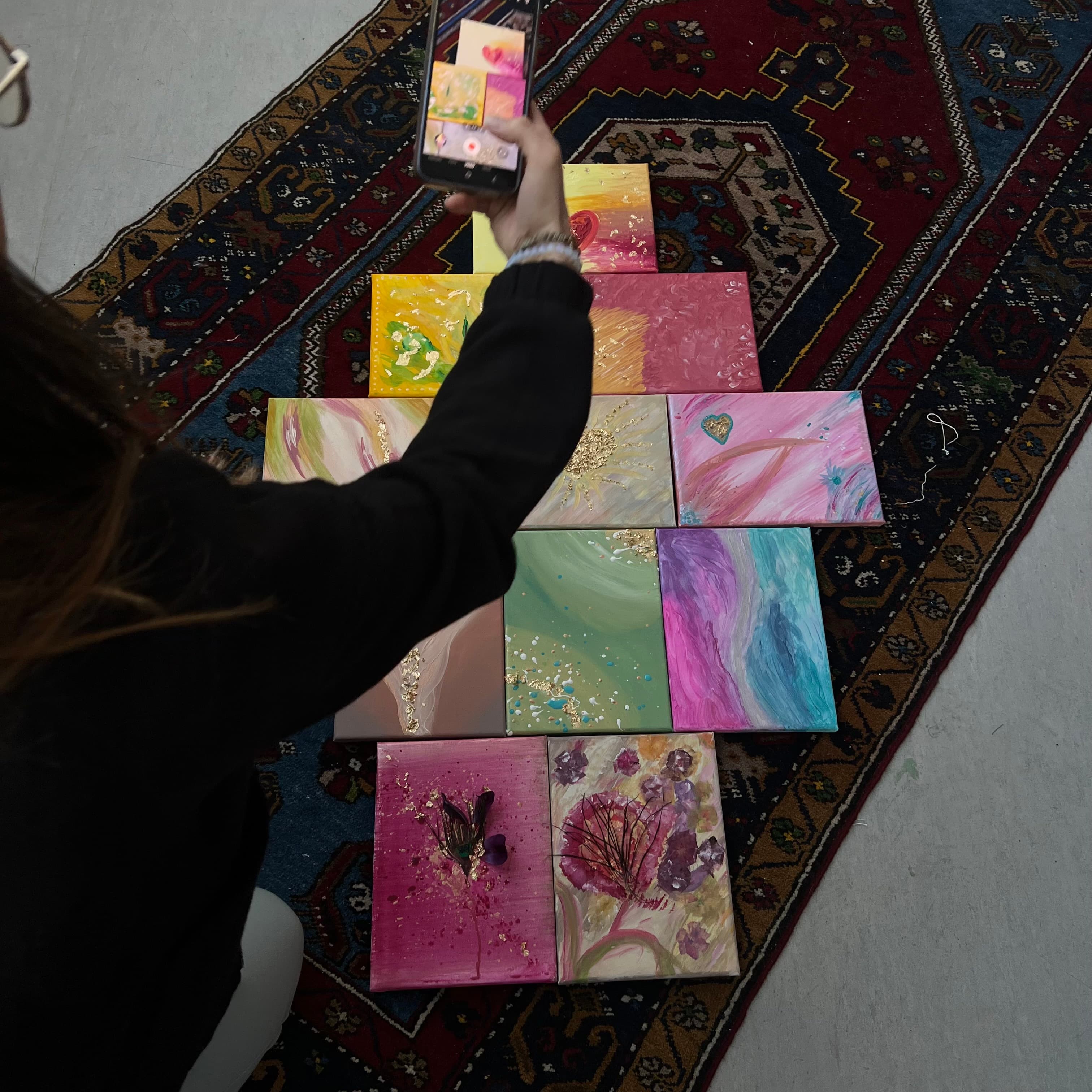Aufsicht auf mehrere fertige Pastell-Leinwände, ausgelegt auf einem Perserteppich im Atelier — eine ganze Gruppen-Session in einem Foto