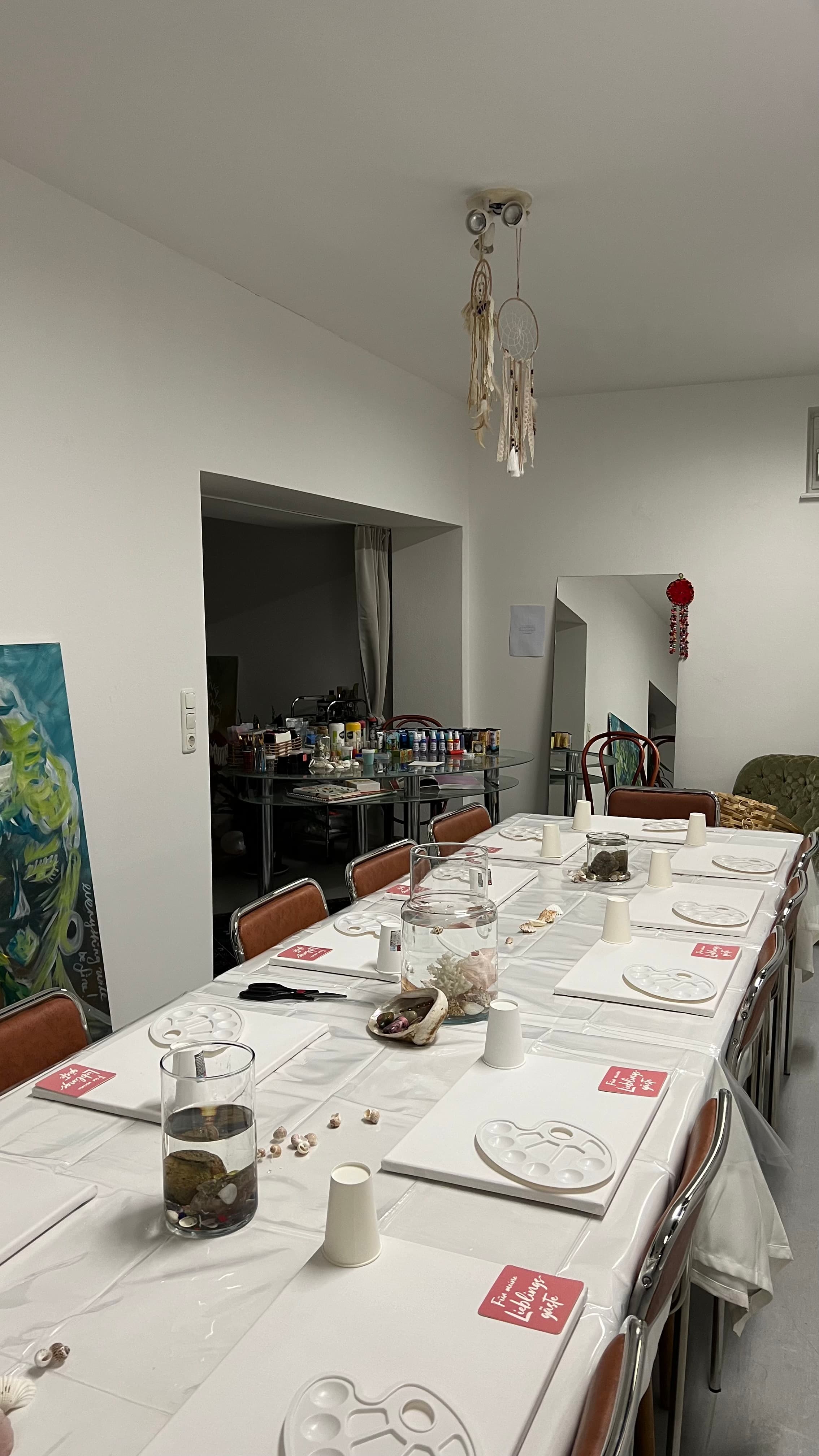 Atelier-Ecke mit langem Tisch, Traumfänger und Staffeleien im Hintergrund